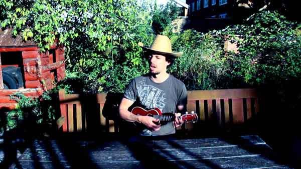Man playing ukulele in the garden with a straw hat on