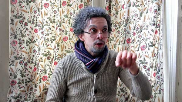 Comedian Elliot Mason as an old man in glasses being interviewed