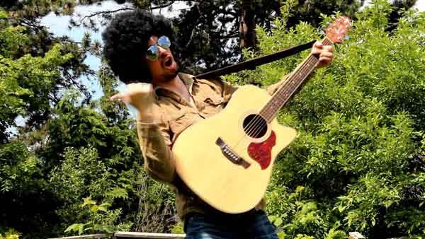 Acoustic guitarist outside with an afro wig